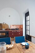 Wooden table with blue-upholstered chairs in front of rustic kitchen counter in arched niche