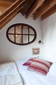Bed in corner of room below oval transom window