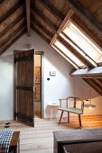 Rustikales Zimmer mit sichtbarem Dachstuhl, schlichter Armlehnstuhl unter Dachfenster