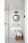 Schmaler Waschbereich, unter Waschbecken rustikaler Schemel mit Handtücher Stapel, neben Glastrennwand vor Dusche