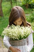 Girl outdoors holding large bouquet of lily-of-the-valley in wicker basket