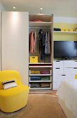 Stauraum im Schlafzimmer durch praktisches Innenleben im Kleiderschrank; gelber Sessel als sonniger Akzent vor neutralem Weiß