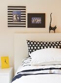 Schwarzweisser Mustermix auf Kissenbezügen, dekorativen Bilderrahmen und Deko-Katze über dem Bett