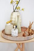 An arrangement featuring vases, wooden rabbits and gilded porcelain beetles on a wooden tray on a wooden table