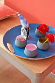 A set of bowls and a porcelain budgerigar on a cornflower blue tray against a coral-coloured wall