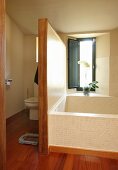 Badewanne vor Fenster mit Sichtschutzpaneel an der Seite und Toilette im Hintergrund