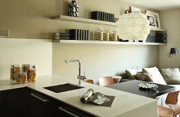 View across white counter with fitted sink in front of dining area below designer pendant lamp in open-plan interior