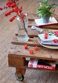 Branch of red berries in vase and red dice on coffee table made from wooden pallet and castors