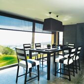 Black and white designer dining area next to continuous glass wall with view of landscape