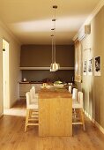 Langer Esstisch aus Holz und weiße, gepolsterte Barhocker vor Küchenzeile