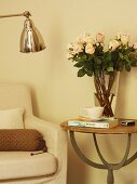 Glass vase of roses on delicate side table next to armchair; partially visible retro, chrome standard lamp