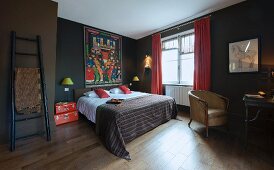 Dunkelbraun getöntes Schlafzimmer mit buntem Mandarin-Bild über Doppelbett, rote Koffer als Nachttisch