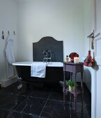 Clawfoot bathtub and small table in bathroom with black marble floor