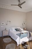 Double bed flanked by shabby-chic bedside cabinets and wall lamps; fan on stucco ceiling