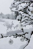 Two wooden deer figurines and white Christmas baubles on snow-covered branch