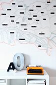 Stylised, string-art map of city decorating wall, orange retro typewriter and ornamental letter on white shelf