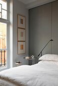 Bed with white bed linen against floor-to-ceiling panels covered in grey fabric in traditional, elegant interior