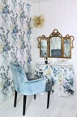 Armlehnstuhl mit hellblauem Samtbezug vor Schminktisch mit Husse und nostalgischem, dreiteiligem Spiegel an weisser Holzwand