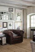 Brown leather armchair below collection of artworks on wall in rustic interior