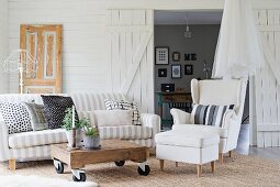 Weisser Polsterhocker, Sessel und Sofa um rollbarem Holztisch im Wohnzimmer mit weisser Holzverkleidung