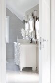 Bright bathroom; vintage chest of drawers painted white with modern countertop basin below carved mirror and stainless steel sconce lamps