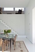 Essplatz mit modernem Tisch mit Glasplatte, im Hintergrund Treppenaufgang mit minimalistischem Geländer