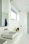Washstand with white, minimalist base unit below tall narrow mirror next to window