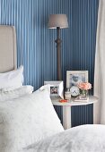 Framed photos, vintage alarm clock and bedside lamp on bedside table against blue and white striped wallpaper