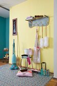 Retro cleaning utensils on patterned rug in front of coat rack on pale yellow hall wall
