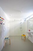 Spacious bathroom with twin sinks, colourful classic stools and floor-level shower with glass screen in background