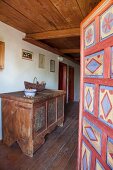 Blick von offener, bemalter Tür auf Holztruhe mit Bauernmalerei im Hausflur eines restaurierten Bauernhauses