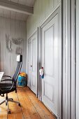 Modern office chair on rustic wooden floor in room with wooden walls painted pale grey