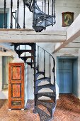 Black, hand-crafted vintage spiral staircase on herringbone terracotta floor in rustic country house with historical ambiance