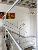 Blick von Galerie auf gemauerten Treppenabgang mit Metall Geländer, weisses Sofa in offenem Wohnraum mit Kassettendecke aus Beton