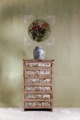 Vintage chest of drawers with fronts covered in wallpaper below decoupage picture applied to wall