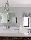 White, modern washstand with twin sinks, mirrored cabinet and half-height, exposed brick wall in modern, country-style bathrom