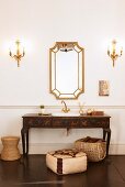 Antique, painted washstand and framed mirror flanked by candle sconces above pouffe and basket on dark floor