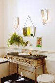 Antique, Rococo-style washstand and vintage mirror flanked by candle sconces in old-fashioned bathroom
