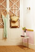 Dress hung on door of 50s-style fitted wardrobe, vase of flowers on small side table and sisal carpet in nostalgic interior
