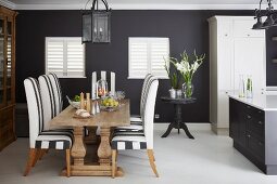 Open-plan kitchen with dining set in front of black-painted wall and closed interior shutters on windows