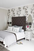 Bedside cabinets flanking double bed with tall headboard against wall covered in floral wallpaper