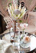 Protea in vintage apothecary bottle and roses in small crystal vases on glass table