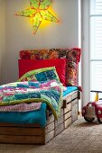 DIY bed made from wooden crates with colourful patchwork blankets below glowing, star-shaped lamp