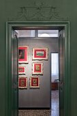 View through door with green stucco to hallway with antique picture gallery