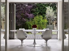 White, classic Tulip Table and matching chairs in front of open folding chairs with view into garden