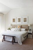 Bright bedroom with button-tufted headboard, white-framed drawings and rustic vintage bedroom bench