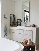 Blick über Badewanne auf gemauerten Waschtisch mit eingebautem Unterschrank in Weiß