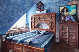 Bed with carved wooden frame and Oriental-style headboard in attic room with mottled blue walls