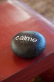 Black stone decorated with lettering reading 'calme' on red-painted table