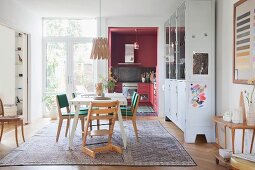 Tripp Trapp highchair and retro chairs around white table on rug in rustic dining room: dusky-pink fitted kitchen in background